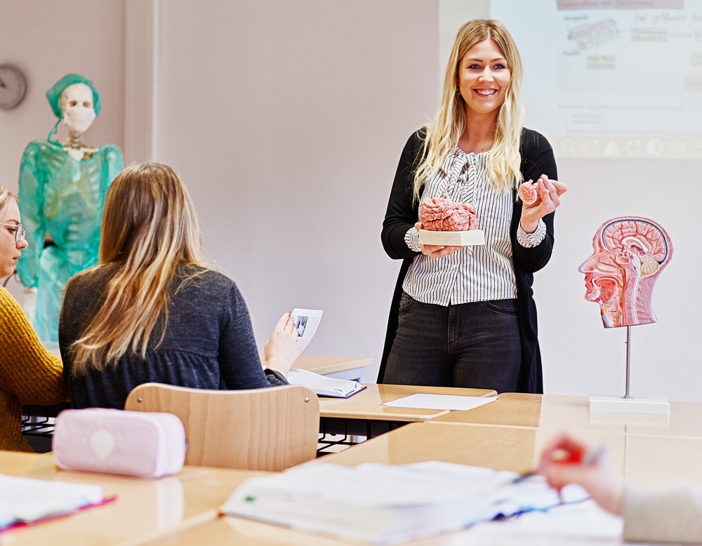 Eine Lehrerin hält ein Lehrobjekt in der Hand und spricht zu den Schülerinnen und Schülern.