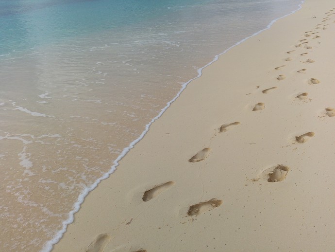 Am Strand sind direkt neben dem Meer die Fußspuren von zwei nebeneinander laufenden Menschen in den Sand gedrückt